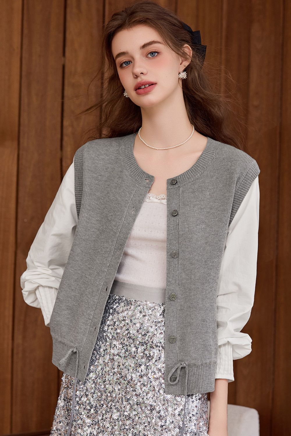 Model wearing a gray knit button-front vest over a white blouse and floral skirt