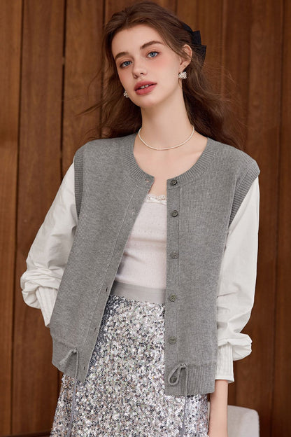 Model wearing a gray knit button-front vest over a white blouse and floral skirt