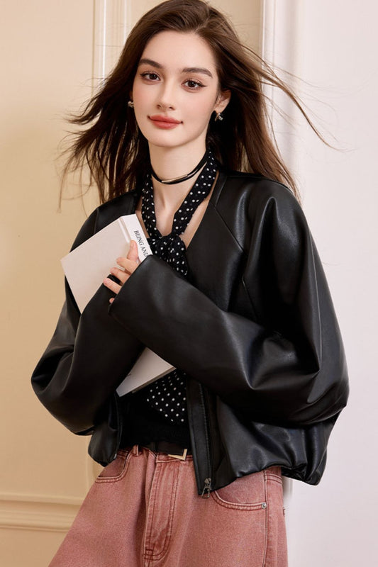 Front view of woman wearing a black faux leather jacket over a polka dot blouse with pink pants