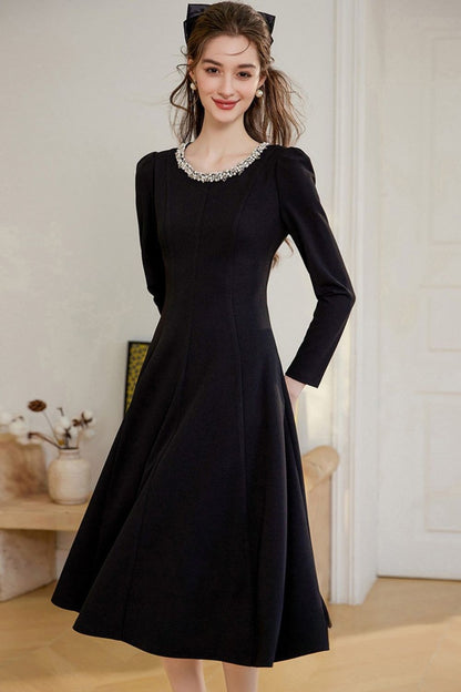 Model wearing a long-sleeve black midi dress, standing with one hand behind her back