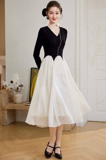 Model wearing a black long-sleeve top with a white flared midi skirt, standing in a room