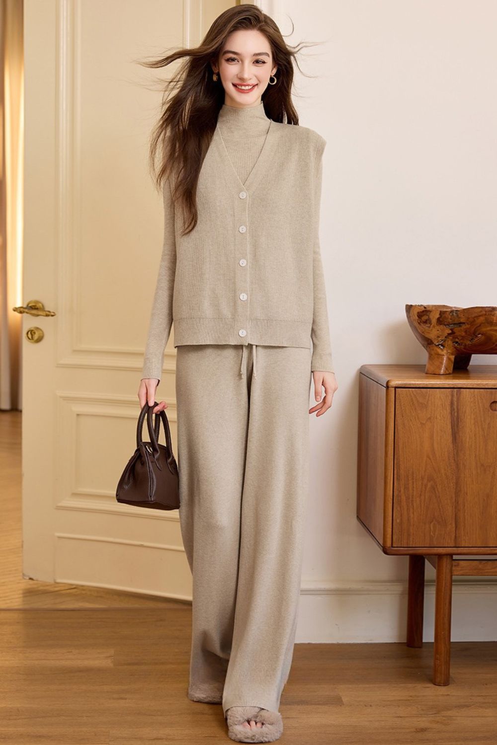 Full-body view of model in beige knit set with relaxed silhouette, holding a handbag