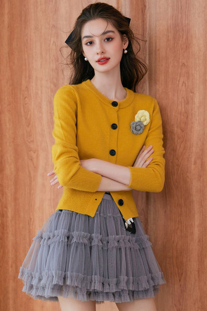 Front view of mustard yellow cardigan with flower detail and gray pleated skirt