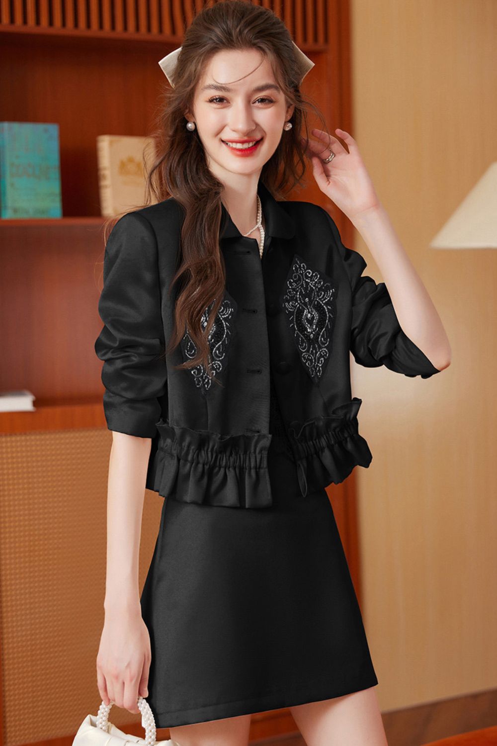 Smiling model in black embroidered tassel jacket and black skirt holding a handbag