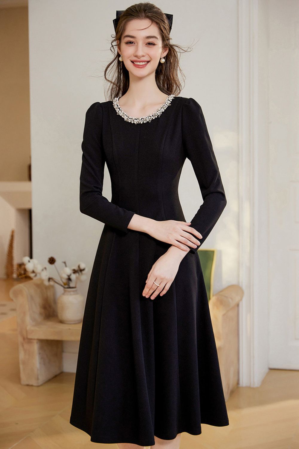 Front view of black midi dress styled with pearl necklace and clutch bag