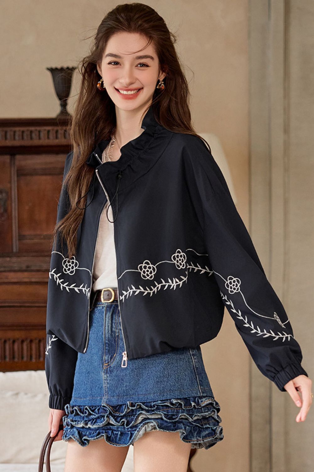 Side view of model in black embroidered jacket paired with a denim mini skirt