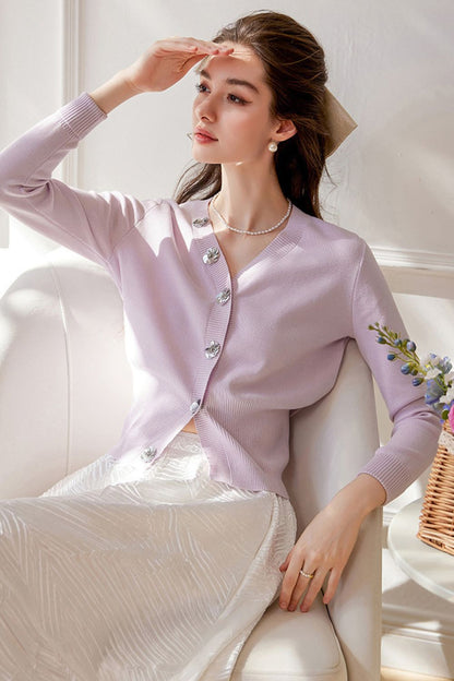 Seated pose of model in light purple pearl-button cardigan and white skirt