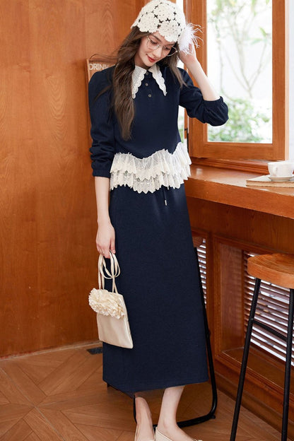Model leaning on a table wearing navy blue lace-trimmed blouse with navy skirt and crochet hat