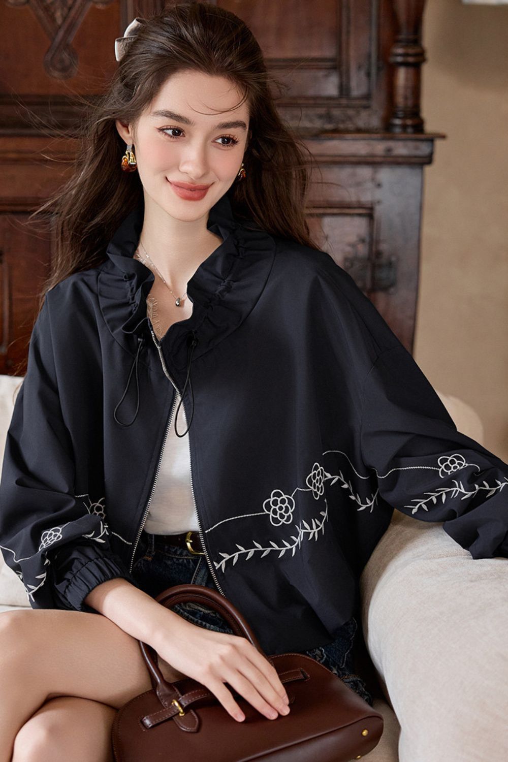 Close-up of model sitting, showing details of the embroidered black jacket