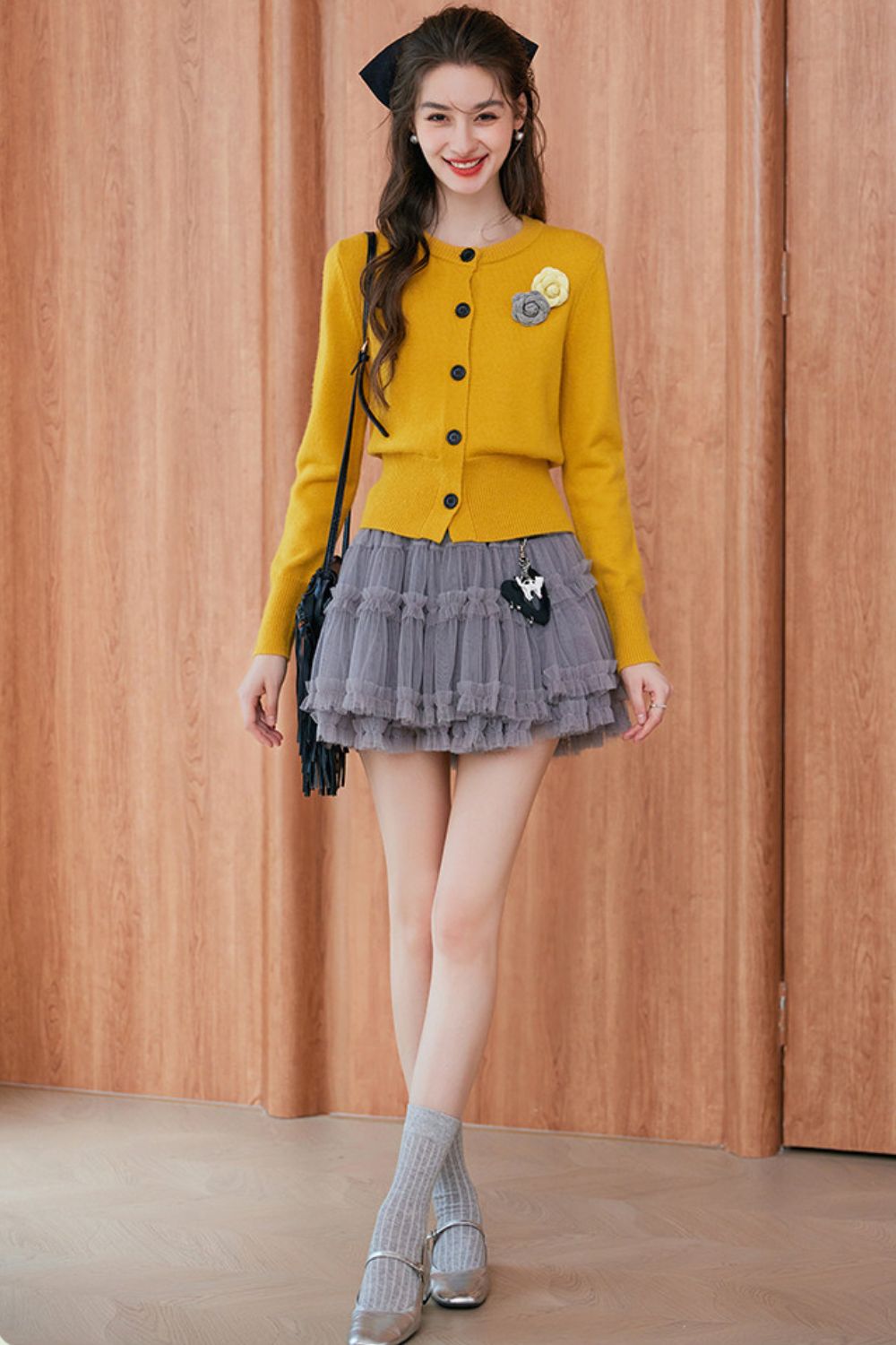 Standing pose of model in mustard yellow cardigan with brooch and gray skirt