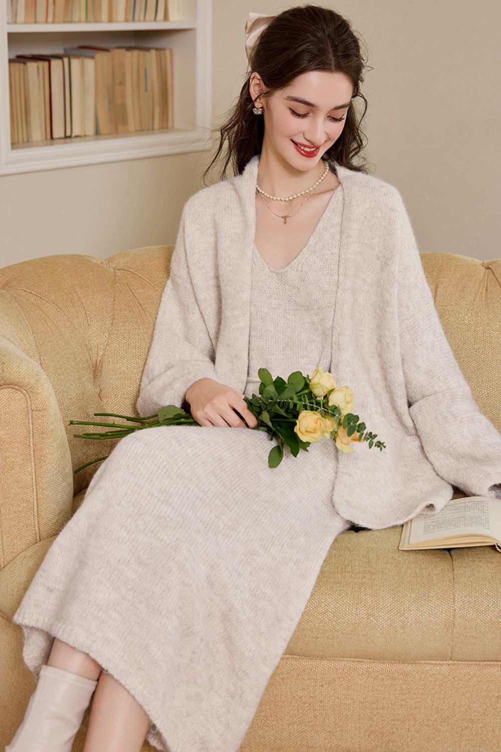 Side angle of a woman in a cream knit cardigan dress carrying flowers