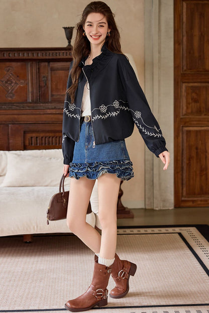 Walking pose of woman in black embroidered jacket, denim skirt, and boots