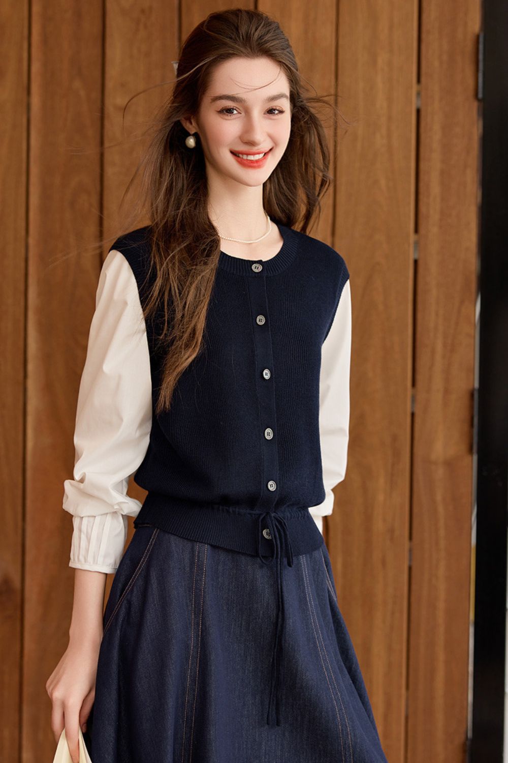 Model wearing a navy blue knit vest over a white blouse and long navy skirt