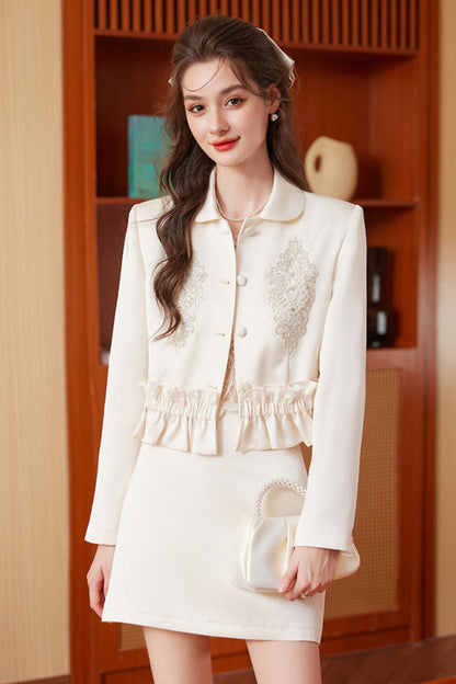 Model in cream embroidered tassel jacket with cream mini skirt, standing and posing