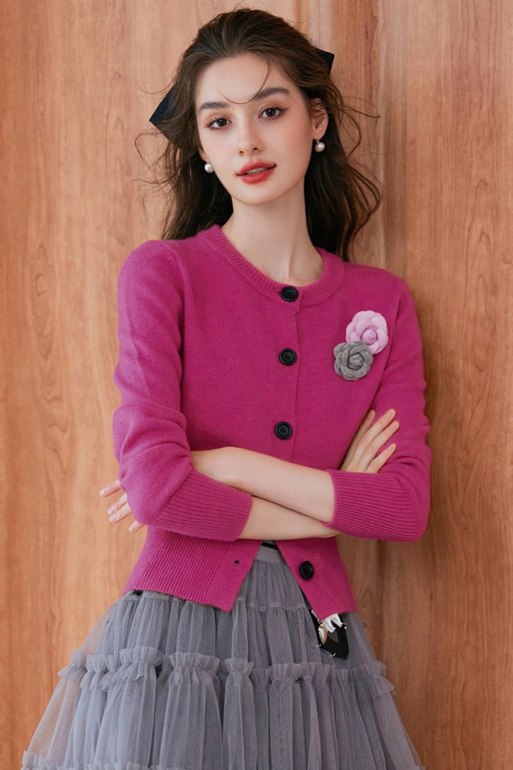 Front view of pink buttoned cardigan with floral brooch, styled with gray pleated skirt
