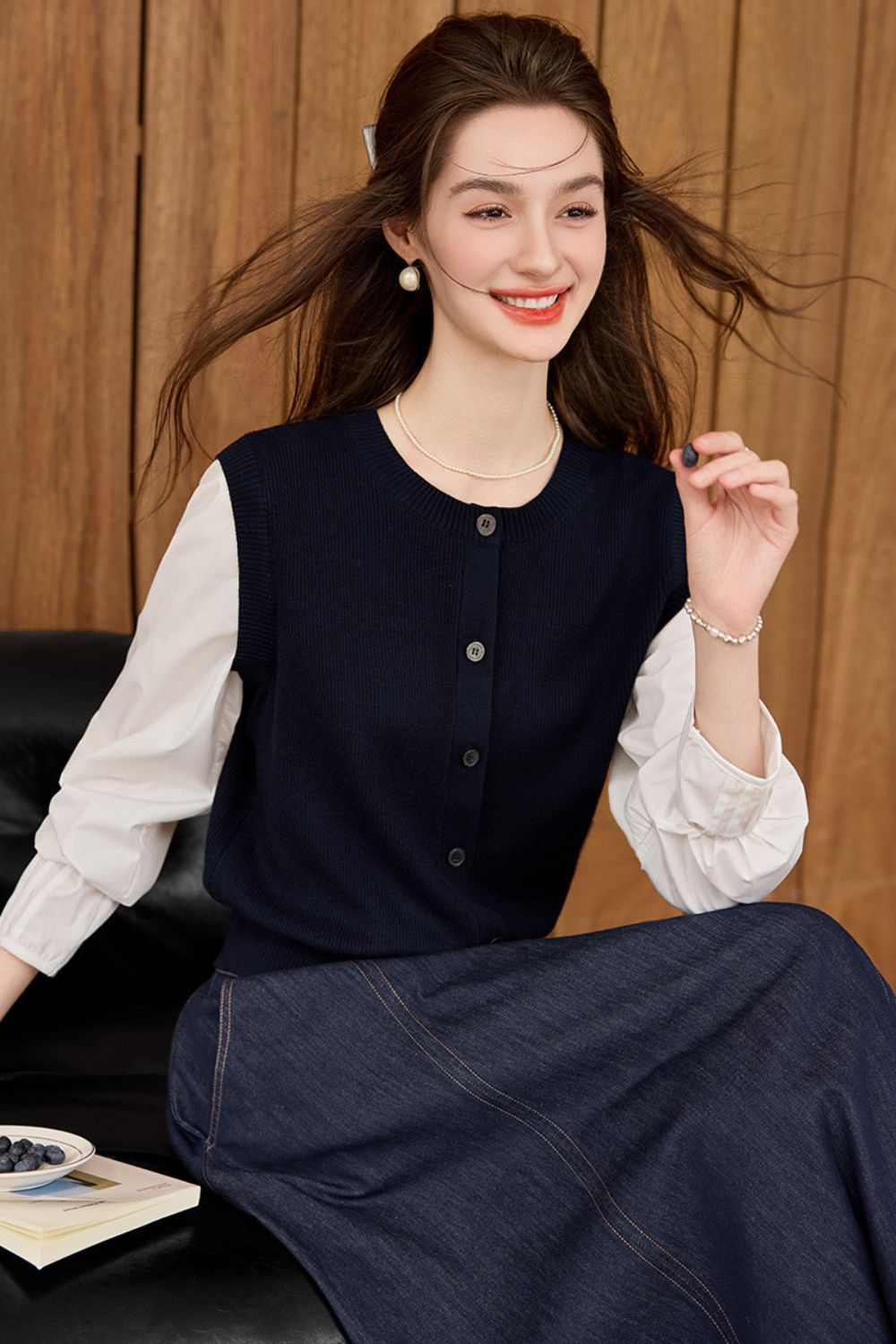 Navy blue vest layered over a white blouse and navy skirt, side view while seated